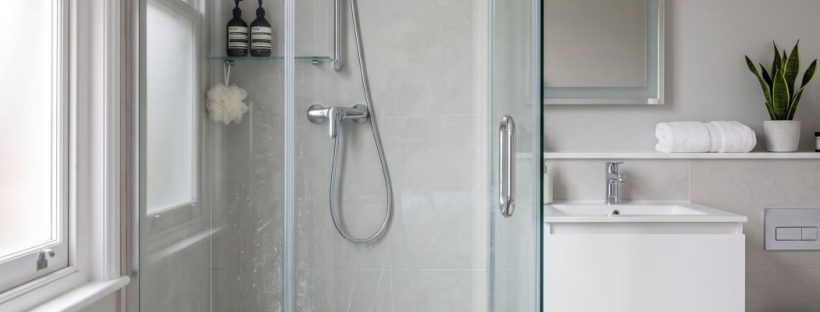 a frameless tempered glass shower door with subtle but clearly visible hard-water residue, faint limescale spotting, light soap scum haze, and delicate mineral streaks that have naturally built up over time